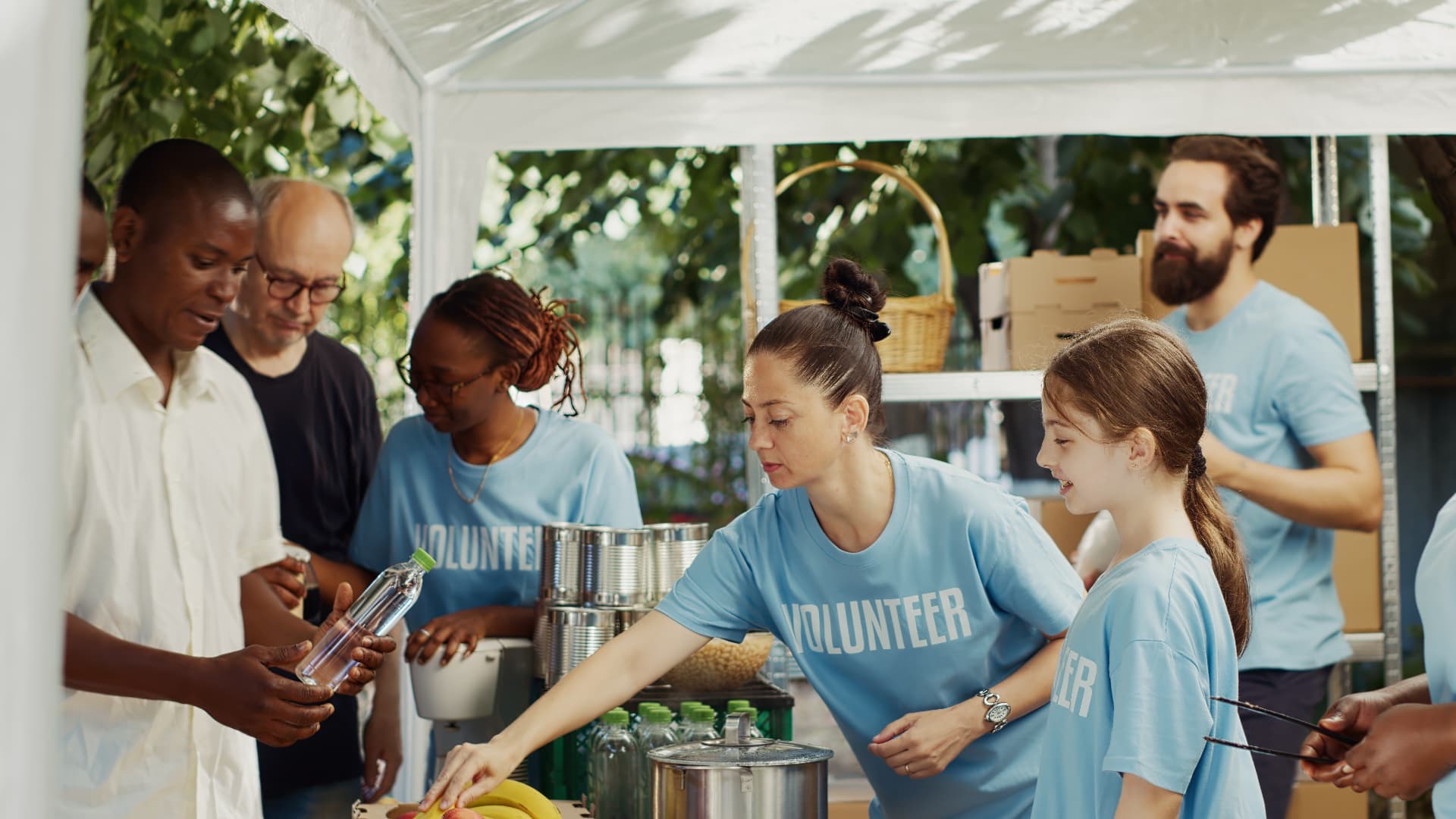 Volunteers in blue shirts serving water, canned goods and fruit to neighbours at an outdoor distribution table.